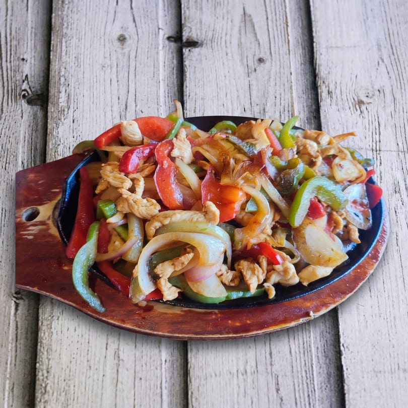 Sizzling chicken fajitas with red and green bell peppers and onions on a dark platter.