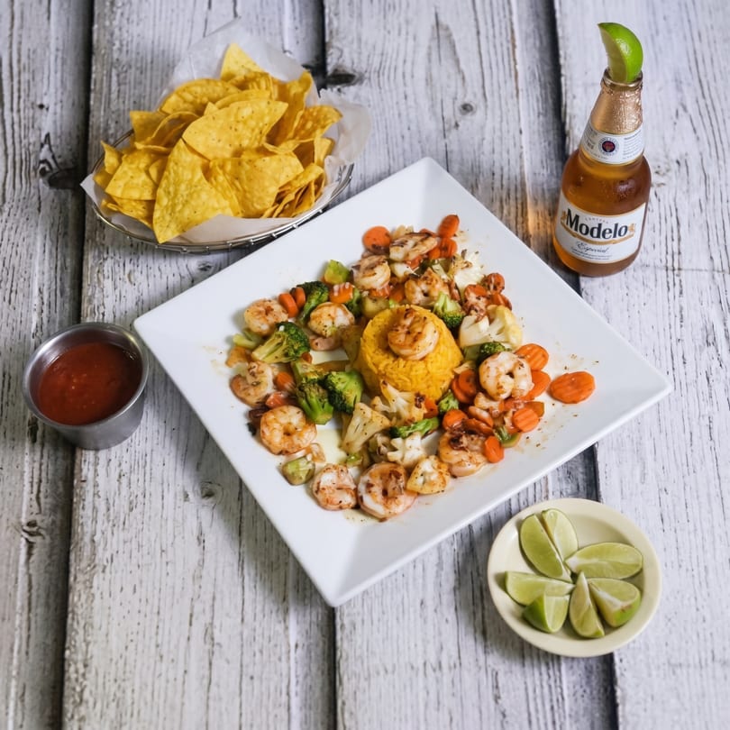 Shrimp and vegetable stir-fry with yellow rice, tortilla chips, salsa, lime wedges, and a beer.
